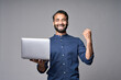 © insta_photos - Happy excited indian business man employee holding laptop computer standing isolated on gray background celebrating win, good online results, business success, job promotion or achievement concept.