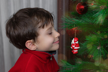 Close-up happy little boy in a red jacket looking with curiosity at a Christmas tree toy 