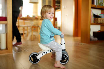 Funny toddler boy riding a baby scooter at home. Kid training balance on mini bike indoors.