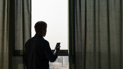 Silhouette of a man with mobile phone at the window. Concept