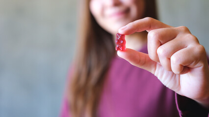 Wall Mural - Closeup image of a young woman holding and showing at a red jelly gummy bear