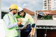 © thanmano - Engineer and Contractor wearing helmet and vests are using a computer to look at a building project at a construction site