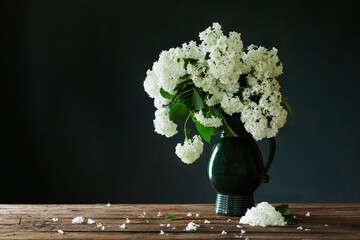 white hydragea in vintage jug on wooden table on background dark wall