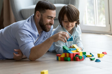 happy dad teaching curious cute son kid to build toy forecast, castle, tower model from colorful blo