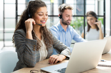 Sticker - Female customer support operator with headset and smiling, with collegues at background.