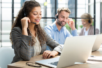 Sticker - Female customer support operator with headset and smiling, with collegues at background.