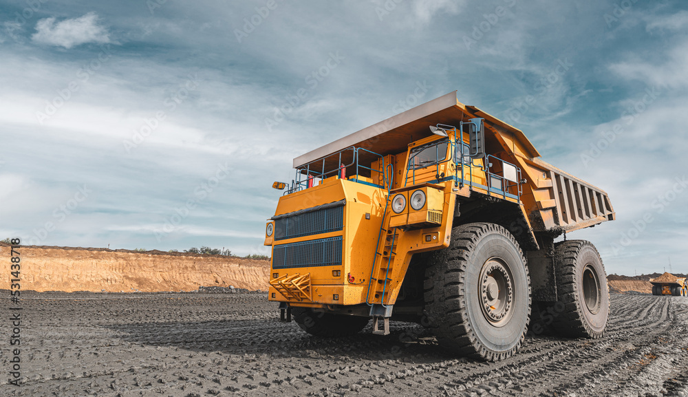 Large quarry dump truck. Big yellow mining truck at work site. Loading coal into body truck. Production useful minerals. Mining truck mining machinery to transport coal from open-pit production
