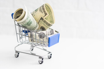 A small shopping cart with 100 dollar bills on a table with space for text.