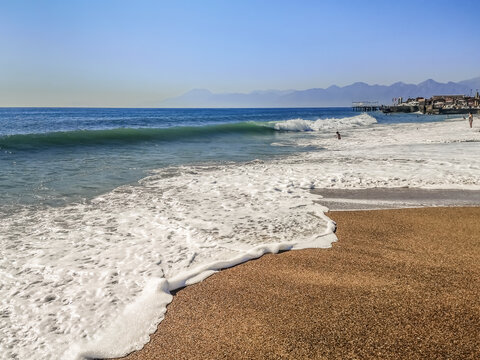Surf with big waves and white foam at Lara beach in Antalya, Turkey. Exotic seascape on a beach with coarse yellow sand