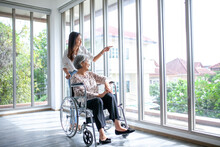 Beautiful Asian Girl Help And Take Care Of Senior Elderly Woman Sitting On Wheelchair At Living Room In House, Senior Therapy Patient At Home Concept.