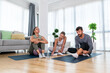 © Srdjan - Young woman fitness and yoga instructor helping couple in their home for workout exercises. Female coach working with clients in their apartment. Husband and wife paying physical therapist for sport.