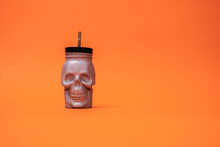 Halloween Drink. Cup In The Shape Of A Skull On An Orange Background With Space For Text. Copy Space. Greeting Card. Bar Invitation. Bar Menu. Alcoholic Drink. Halloween Cocktail