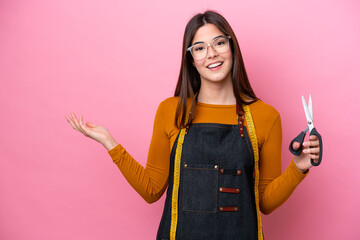 Wall Mural - Young Brazilian seamstress woman isolated on pink background extending hands to the side for inviting to come