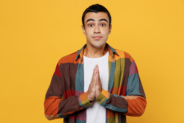 Wall Mural - Young middle eastern man 20s in casual shirt white t-shirt hold hands folded in prayer gesture, begging about something isolated on plain yellow background studio portrait People lifestyle concept