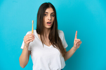 Wall Mural - Young caucasian woman brushing teeth isolated on blue background surprised and pointing side