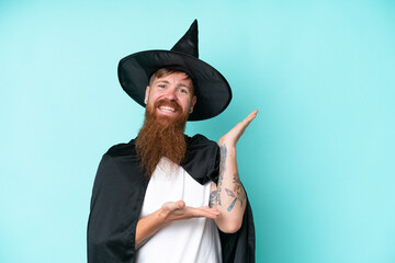 Wall Mural - Young wizard in halloween isolated on blue background extending hands to the side for inviting to come