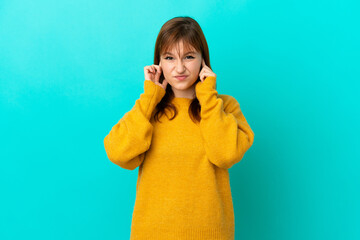 Wall Mural - Redhead girl isolated on blue background frustrated and covering ears