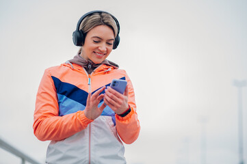 Wall Mural - Young woman taking a break from jogging on the bridge and using smartphone