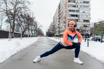 Wall Mural - Woman stretching during her training in the city on a cold winter day.