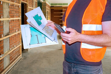 Poster - Man engineer. Architectural drawings in builders hand. Engineer with mobile phone. Builder man calls architectural company. Room architectural plan. Engineer in building under construction