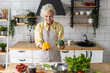 Attractive senior woman with grey hair cooking healthy food on her kitchen at home. Mature female preparing fresh vegetarian salad with organic ingredients from the market: tomato, cucumber, pepper
