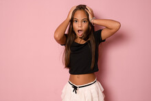 Fun Portrait Of Cute Brunette Kid Girl With Hands On Head.Youngster With Open Mouth And Shocking Facial Expression Isolated On Pink Background.