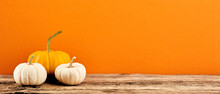 Three Decorative Pumpkins On Wooden Tabletop On Orange Background. Banner Design For Autumn Holidays