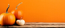 Three Decorative Pumpkins On Wooden Tabletop On Orange Background. Autumn Holidays Banner Design. Thanksgiving, Harvest Concept.