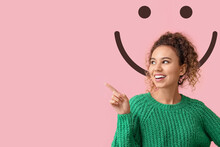 Young African-American Woman Pointing At Something And Drawn Smile On Pink Background