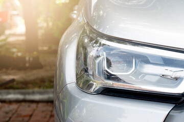 Front headlight of the car parked in the park. Blurred of trees in park area.