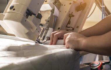 Women's hands in the process of sewing on professional equipment. Sewing fabric in production. Close-up