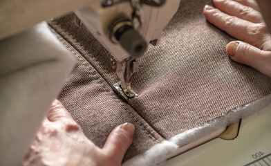 Wall Mural - Women's hands in the process of sewing on professional equipment. Sewing fabric in production. Close-up