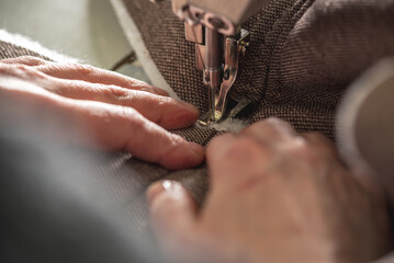 Wall Mural - Women's hands in the process of sewing on professional equipment. Sewing fabric in production. Close-up