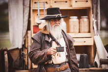 Oldest Smart Cowboy Wearing Western Style With Cowboy Hat Hold A Cup Drinking Coffee On Early Morning Is 1800s Countryside Lifestyle Concept.