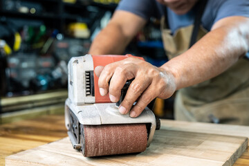 carpenter working with belt sander polishing on wooden in workshop ,DIY maker and woodworking concept. selective focus