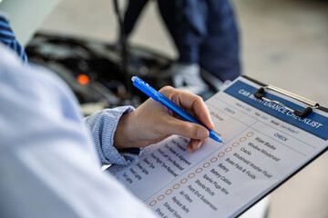 Hand of employee check list to the clipboard insurance while mechanic inspecting car at garage workshop.