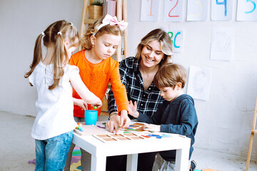 Children with interest play with educational toys on desk sitting on floor. Smiling educator point at empty hole in constructor in playroom. Learning geometric figures, lesson in kindergarten