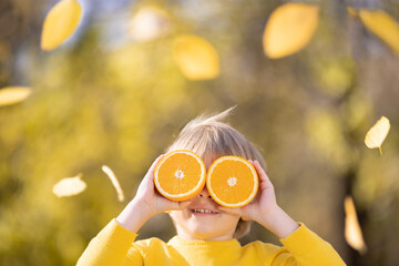 Wall Mural - Surprised child holding slices of orange in autumn park