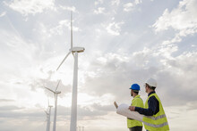 Technicians Looking At Wind Turbines By Clouds In Sky