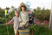 Senior Woman Holding Basket Standing With Grandchildren In Garden