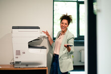 Cheerful Businesswoman Standing By Computer Printer At Workplace