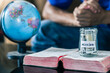 © surachat - Savings jars full of money on bible for mission with a man sitting praying at background, christian concept.