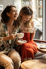 beautiful happy women talking and laughing while drinking coffee together in coffee shop.