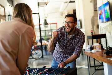 Colleagues having fun at work. Businessman and businesswoman playing table soccer