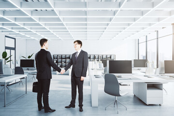 Poster - Businessmen shaking hands in modern concrete coworking office interior with furniture, equipment and window with city view, daylight. Teamwork, success and deal concept.