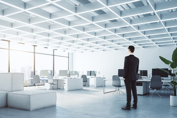 Poster - Businessman standing in modern concrete coworking office interior with furniture, equipment and window with city view, daylight. Worker, CEO and commercial concept.