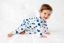 Happy Baby Crawling On Bed Wearing Pajamas With Printed Blue Hearts