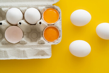 Poster - Top view of natural yolks near eggs in container on yellow background.