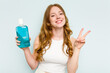 © Asier - Young caucasian woman holding a mouthwash isolated on blue background joyful and carefree showing a peace symbol with fingers.