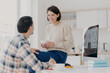 © VK Studio - Indoor shot of happy young woman and man discuss something with drink, use modern computer for making financial report, pose in spacious light room, collaborate together for making common task